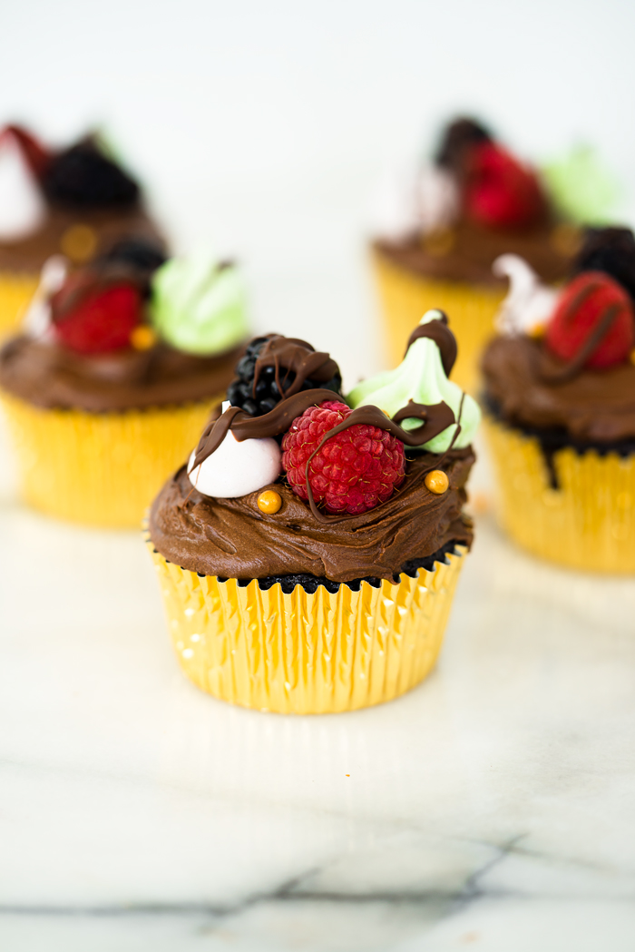 Chocolatey Fudge Cupcake Recipe. Moist, fluffy, pillowy cupcakes in a swirl of fudge chocolate frosting. Decorated in fresh berries and crisp meringues. | thesugarcoatedcottage.com