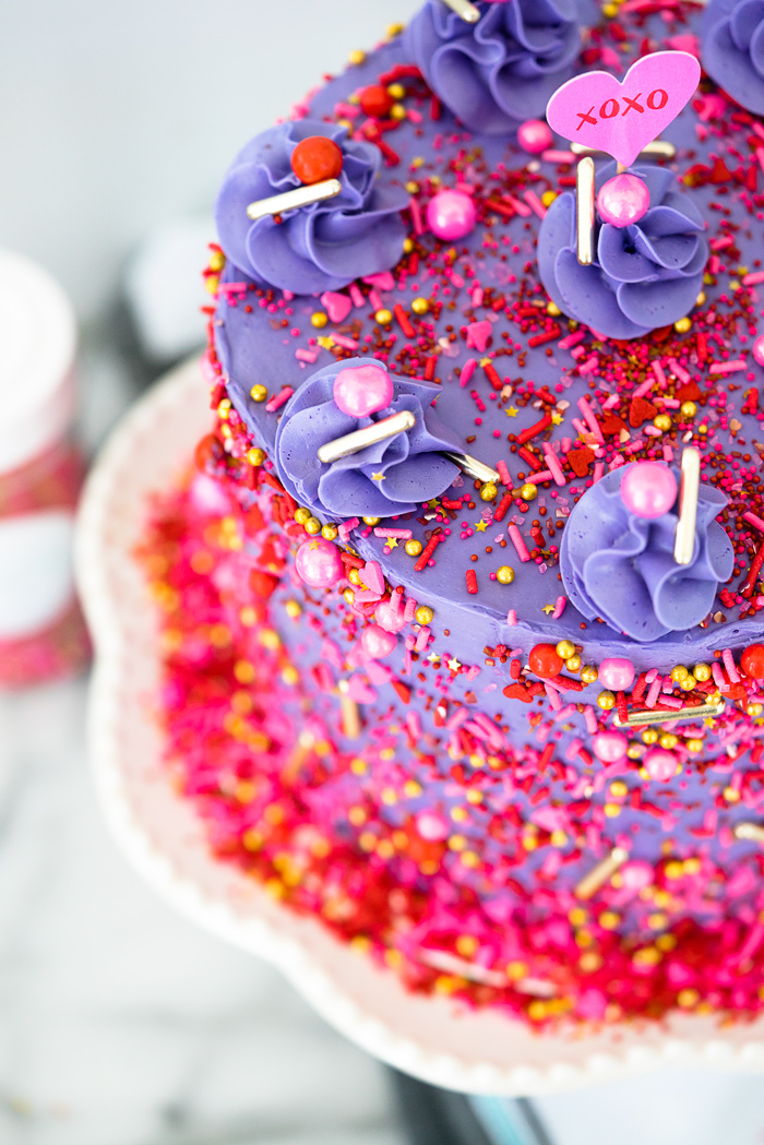 Valentines Red Velvet Cake Recipe. Three layers of southern red velvet cake enrobed in purple swiss meringue buttercream and valentines inspired sprinkles. | thesugarcoatedcottage.com
