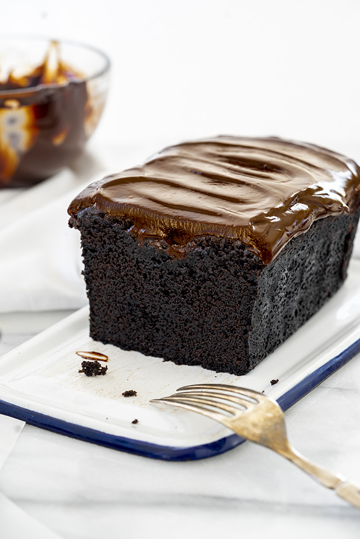 whole chocolate pound cake enrobed in dark chocolate ganache ready to be sliced and eaten. 